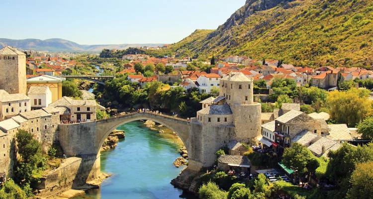 Iconic stone arch bridge spanning a turquoise river with a charming old town and rugged hills in the background.