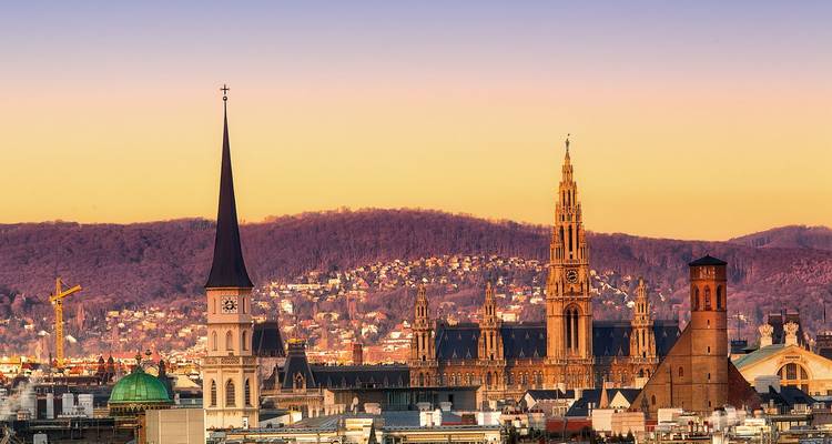 Horizonte de Viena a la hora dorada con agujas de iglesias y el Rathaus neogótico contra colinas de colores pastel.