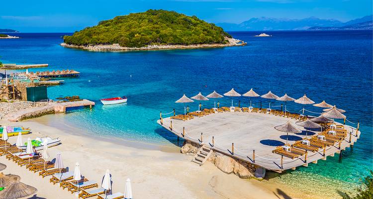 Strand met ligstoelen op een terras omgeven door turquoise water en groen eiland.