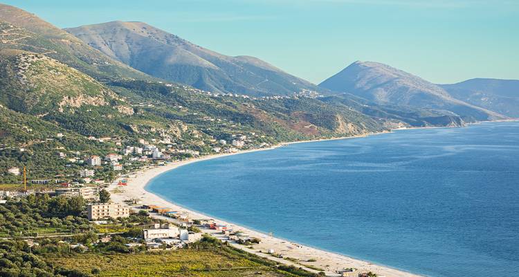 Longue plage incurvée bordée de collines verdoyantes et de petites villes côtières le long de la Riviera albanaise