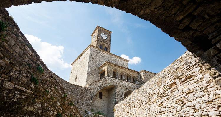 Steinerner Uhrenturm der Festung Gjirokastra, umrahmt von gewölbten Mauern vor einem blauen Himmel.