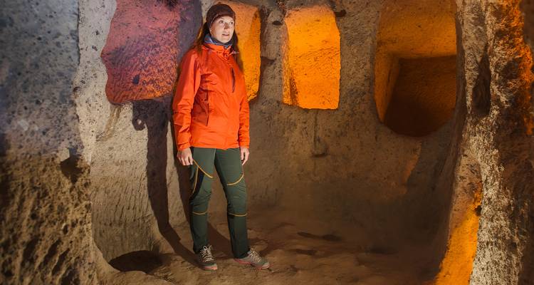 Traveler stands inside an illuminated volcanic-rock chamber of Cappadocia’s underground city.