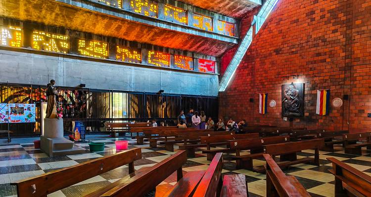 Interior de la Iglesia El Rosario con patrones de luz de vitral super vividos iluminando las paredes de ladrillo y los bancos de madera.