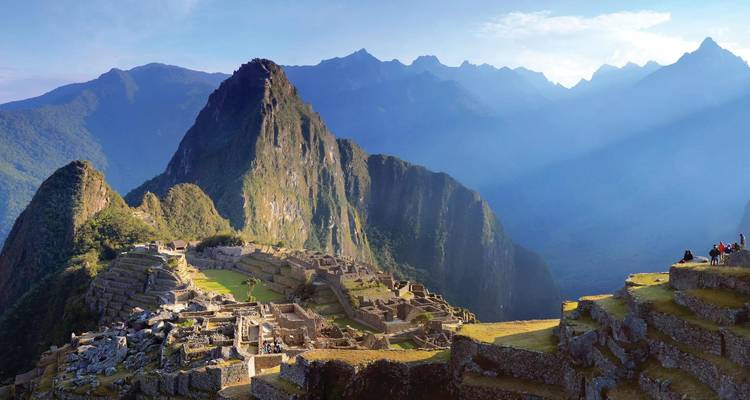 Ikonische Luftaufnahme der Ruinen von Machu Picchu hoch oben inmitten der dramatischen grünen Anden bei Sonnenaufgang.
