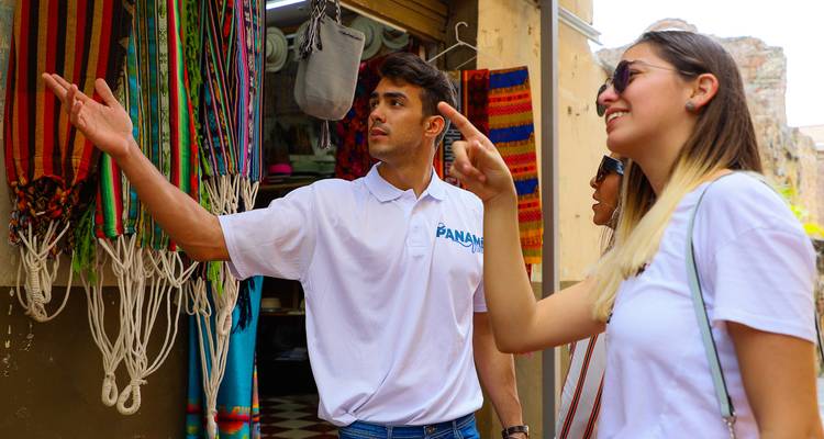 El guía y el viajero señalan las artesanías coloridas que cuelgan en un callejón del mercado.