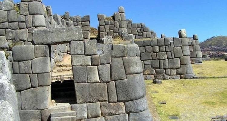 Les énormes murs de pierre imbriqués de la forteresse inca de Sacsayhuamán sous un ciel bleu dégagé.