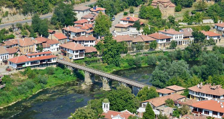 Aerial view of Veliko Tarnovo’s red-roofed houses and a long stone bridge spanning a river amid greenery