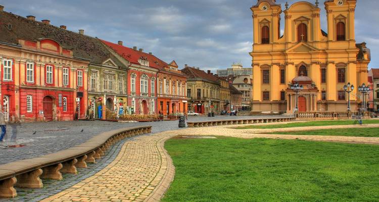 Historic baroque yellow cathedral anchors Timisoara’s colourful main square lined with ornate buildings and green lawns