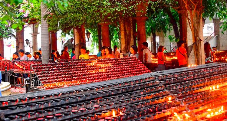 Des dizaines de bougies de dévotion brillent d'une lueur rouge alors que les fidèles allument des offrandes sous des arbres aux feuilles touffues.