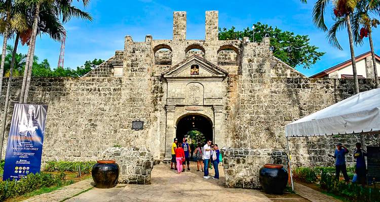 Les visiteurs se tiennent à l'entrée en pierre du Fort San Pedro entourés de palmiers et de ciels dégagés.