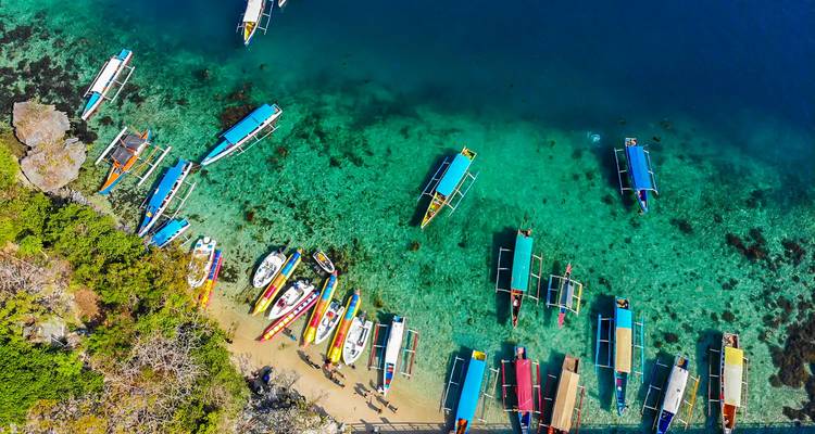 Une vue aérienne de bateaux peints aux couleurs vives ancrés dans une eau aquamarine cristalline près d'un rivage luxuriant.
