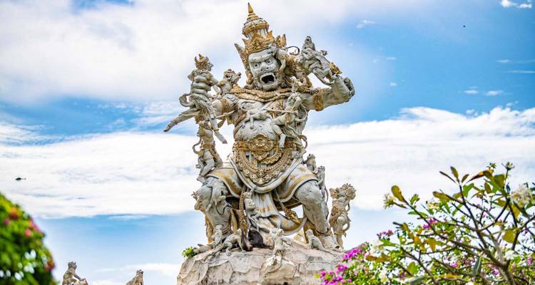 Une statue hindoue spectaculaire en pierre blanche s'élève vers le ciel, entourée d'arbustes fleuris.