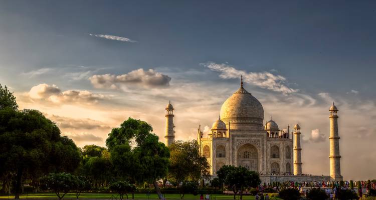 The Taj Mahal at sunset with a crowd of visitors and surrounding greenery.