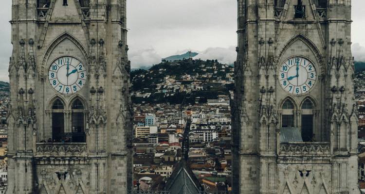 Twee gotische klokkentorens omlijsten een panoramisch uitzicht over het historische centrum van Quito op een bewolkte dag.