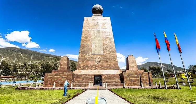 Monument Equator Mitad del Mundo met vlaggen en helderblauw lucht, gedeeld door de gele breedtelijn.