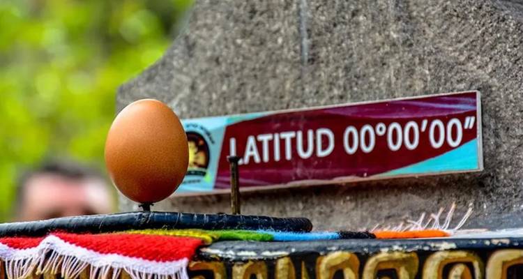 Close-up van een ei dat balanceert op een spijker naast een bord met de tekst "Latitud 00°00'00".