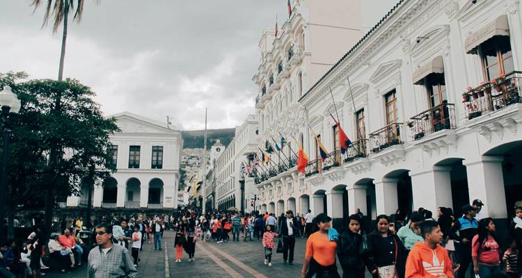 Drukke koloniale plaza omgeven door witte overheidsgebouwen en veel voetgangers in Quito.