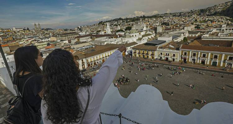 Twee vrouwen op een dakterras wijzen naar Quito's historische skyline en pleinen hieronder.