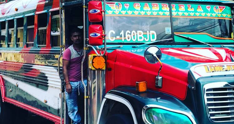 Een kleurrijke Guatemalteekse kipchenbus met gedurfde patronen en chromen details wacht met een passagier in de deuropening.