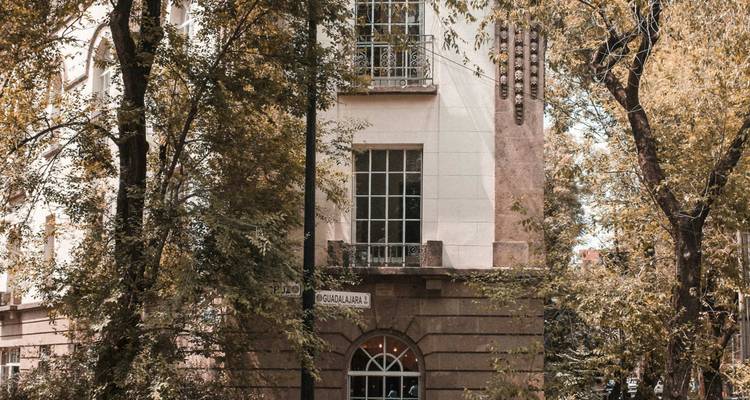 Bâtiment d'angle de charme au style art-déco ombragé par de grands arbres feuilllus dans un quartier résidentiel.