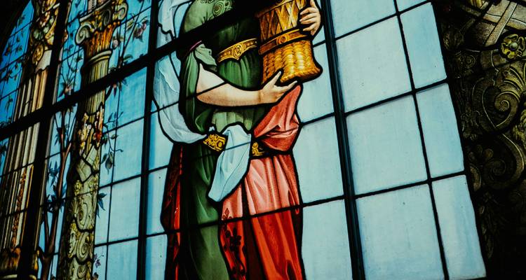 Panneau en vitrail détaillé représentant une figure féminine classique à l'intérieur d'un bâtiment historique.