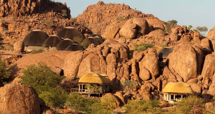 Hütten mit Strohdächern, umgeben von großen Felsformationen.