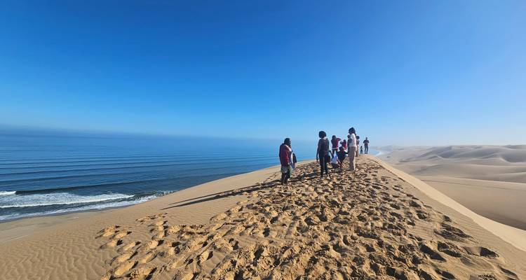 Menschen, die entlang eines sandigen Kamms mit Meerblick unter einem klaren blauen Himmel wandeln.