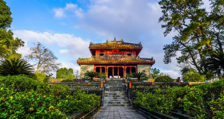 Temple vietnamien traditionnel élégant entouré de jardins luxuriants sous un ciel partiellement nuageux.
