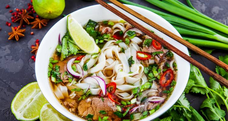 Primer plano de un cuenco humeante de pho vietnamita decorado con lima, hierbas y chile.