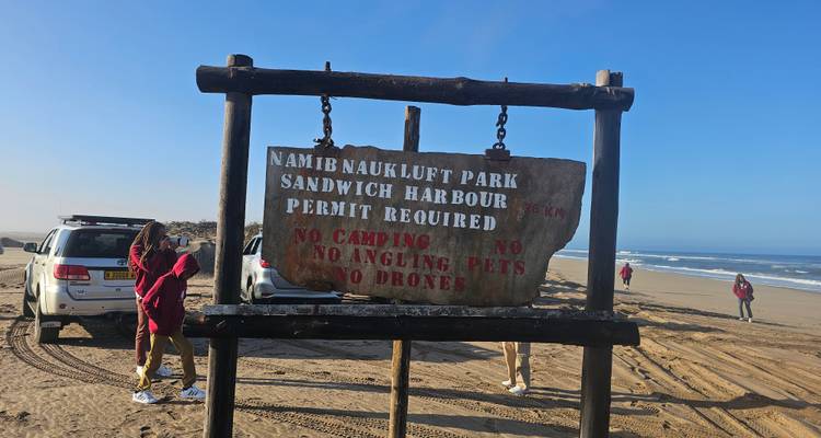 Menschen in der Nähe eines Parkschildes mit sandigem Strand und Ozean im Hintergrund.