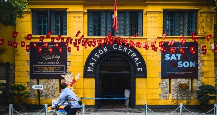 Maison Centrale entrance with flags and a person cycling.
