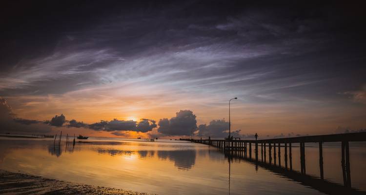 Un atardecer pintoresco sobre un mar en calma con un muelle largo de madera que se extiende hacia el agua.