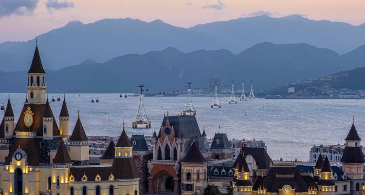 A picturesque coastal view with medieval-style buildings and distant mountains.