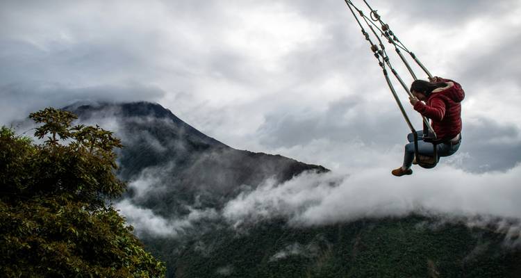 Un joven viajero se lanza sobre laderas montañosas brumosas y nubes, creando una escena de aventura dramática.