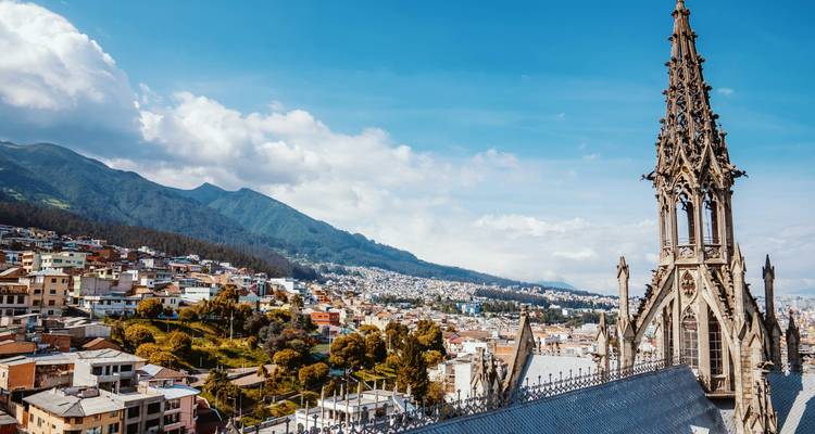 La aguja de piedra de la Basílica domina los suburbios del sur de Quito y las colinas verdes bajo un cielo despejado.