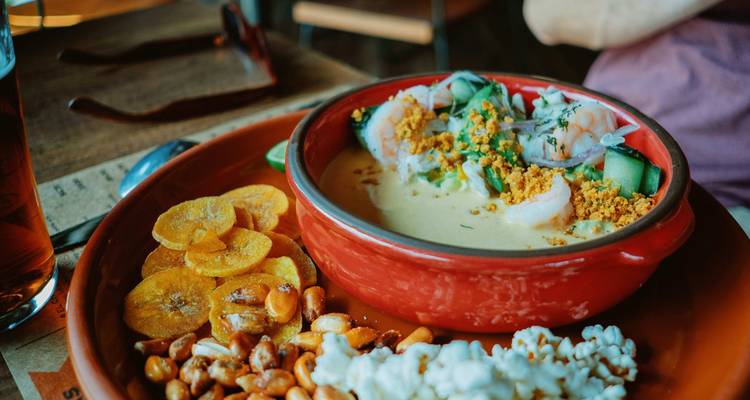 Primer plano de una tradicional sopa de camarones ecuatoriana servida en un tazón de barro con chips de plátano y acompañamientos.