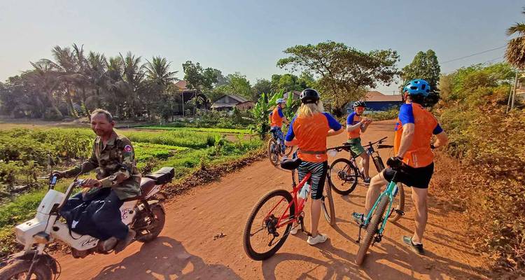 Groupe de cyclistes arrêtés sur une route de terre rouge rurale discutant avec un habitant local sur un motocyclette