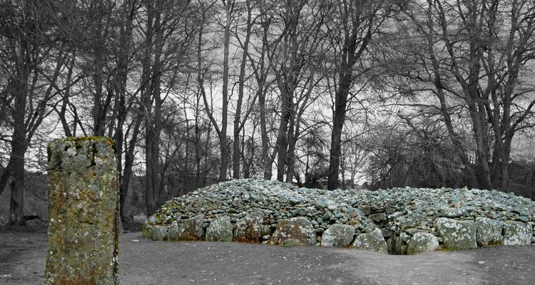 Ancient stone cairn in a bare forest setting.