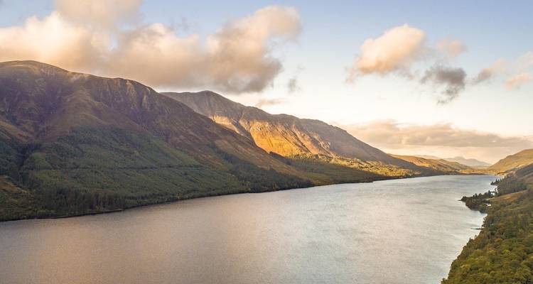 Vue panoramique d'un loch entouré de montagnes au coucher du soleil.