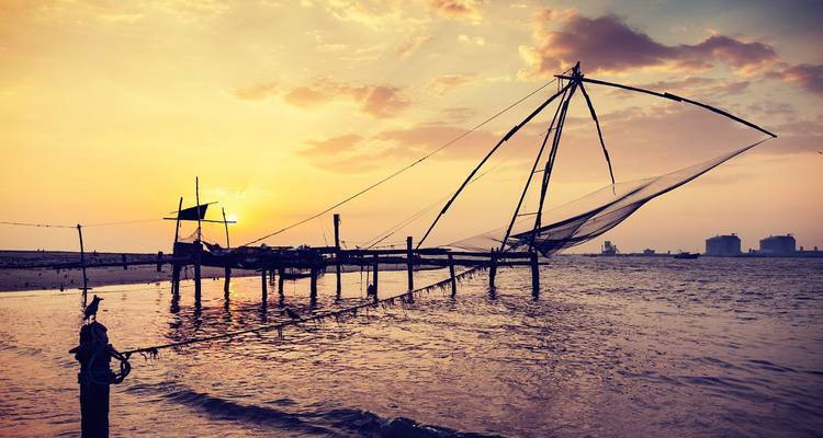 Sonnenuntergang über einem chinesischen Fischernetz in einer ruhigen Strandkulisse.