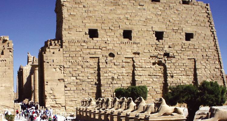 Ingangsmuren van de Karnak-tempel met daarlangs ram-headed sphinx-standbeelden en groepen bezoekers.