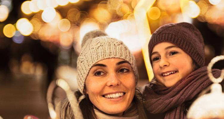 Mère et enfant souriants dans un cadre festif avec des lumières.