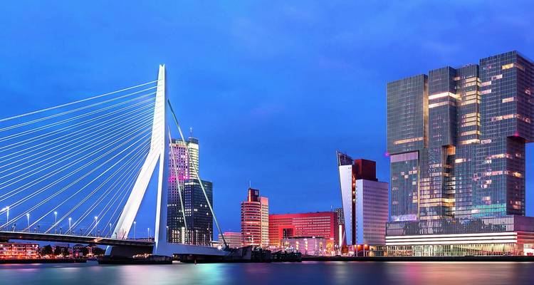 El Puente Erasmus de Rotterdam y su moderno horizonte brillan con luces coloridas al atardecer.