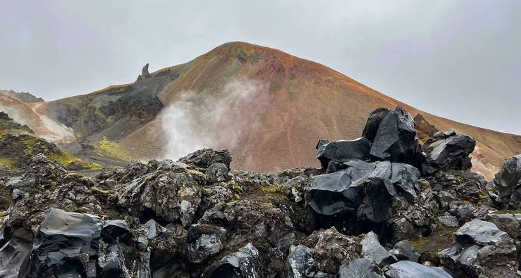 Paysage volcanique fumant avec des roches déchiquetées et des collines colorées.