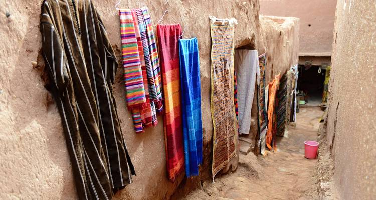 Ruelle étroite en adobe avec des textiles tissés colorés suspendus le long de murs bruts
