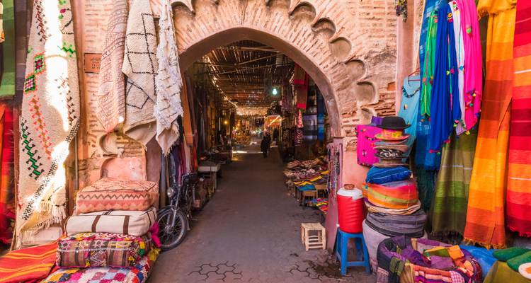 Ruelle du souk aux tissus colorés bordée d'une arche en brique ornementale dans la médina de Marrakech