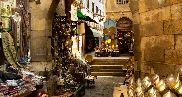 Ruelle étroite du bazar remplie de lampes en laiton, de textiles et de clients au milieu de murs en pierre historiques