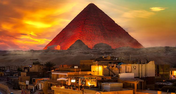 Pyramide illuminée rougeoyant en rouge au coucher du soleil avec des toits de village au premier plan