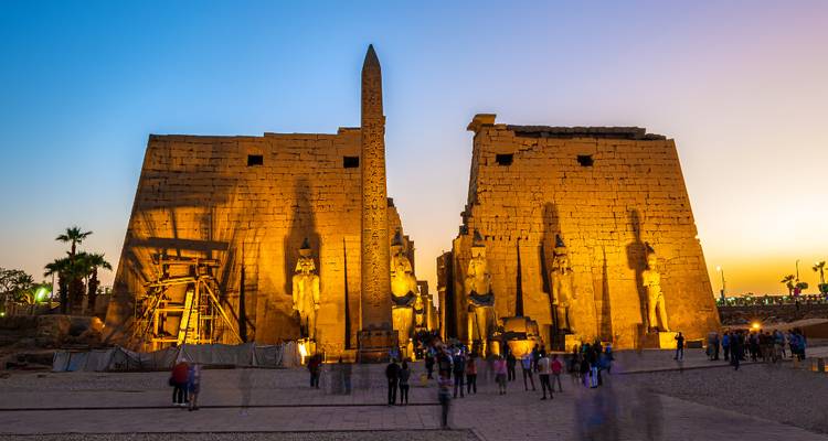 Les lumières du crépuscule illuminent les pylônes colossaux et les statues du Temple de Louxor avec des visiteurs dans la cour