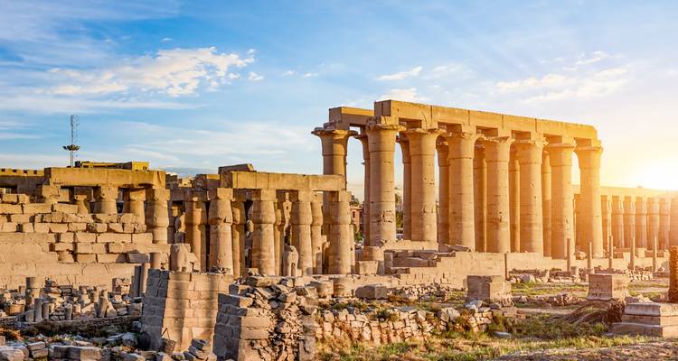 Rangée de colonnes de grès imposantes d'un temple ancien éclairées par le soleil du matin contre un ciel bleu